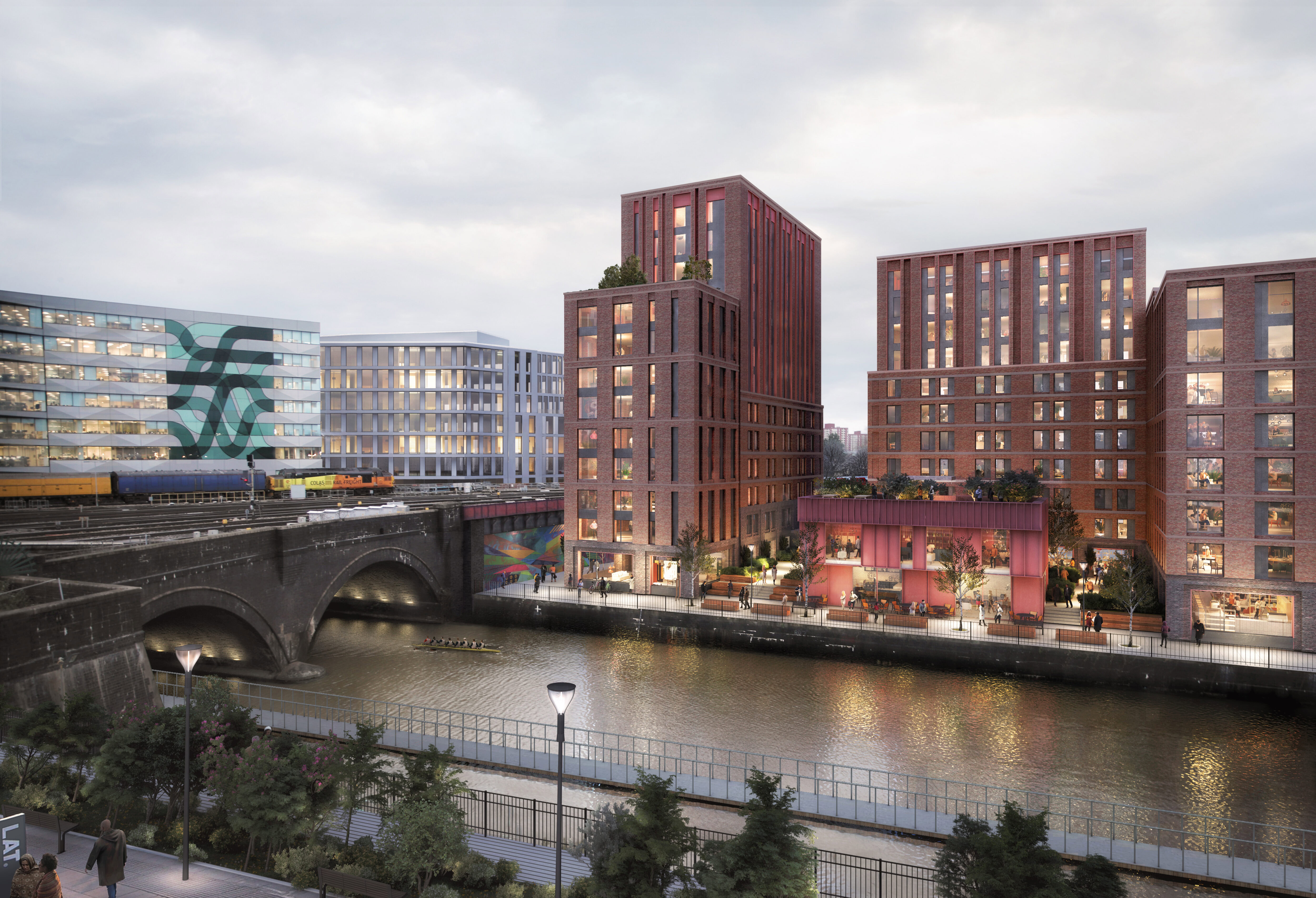 Riverside urban development with modern brick buildings, a railway bridge over a canal, and people walking along the waterfront at dusk.
