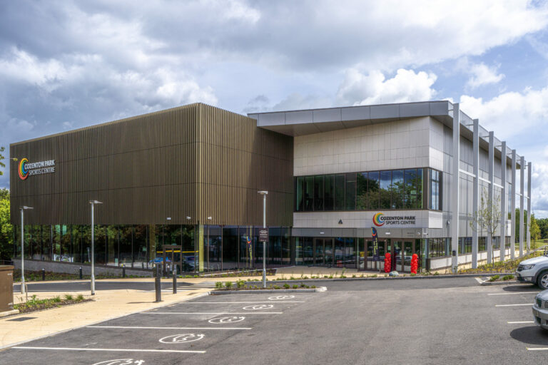 A modern sports centre with large glass panels, set against an overcast sky.