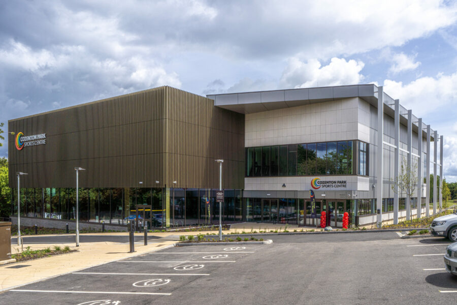 A modern sports centre with large glass panels, set against an overcast sky.