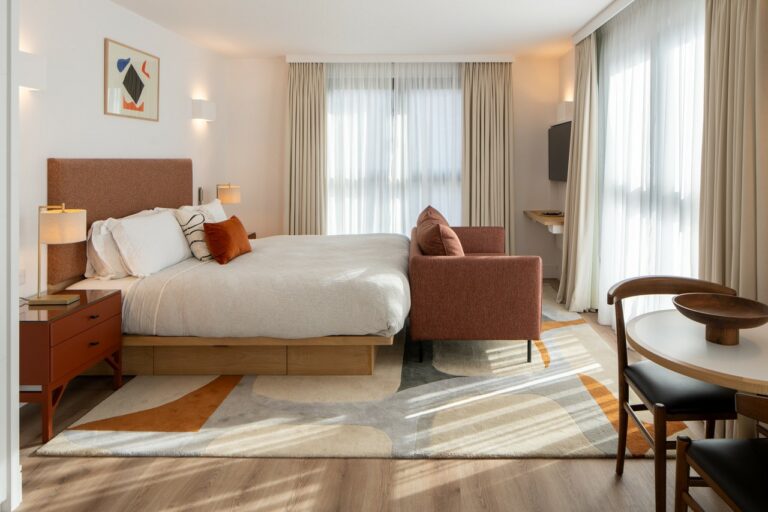 A new and modern hotel room with a large bed, rust-coloured couch, and an abstract rug.