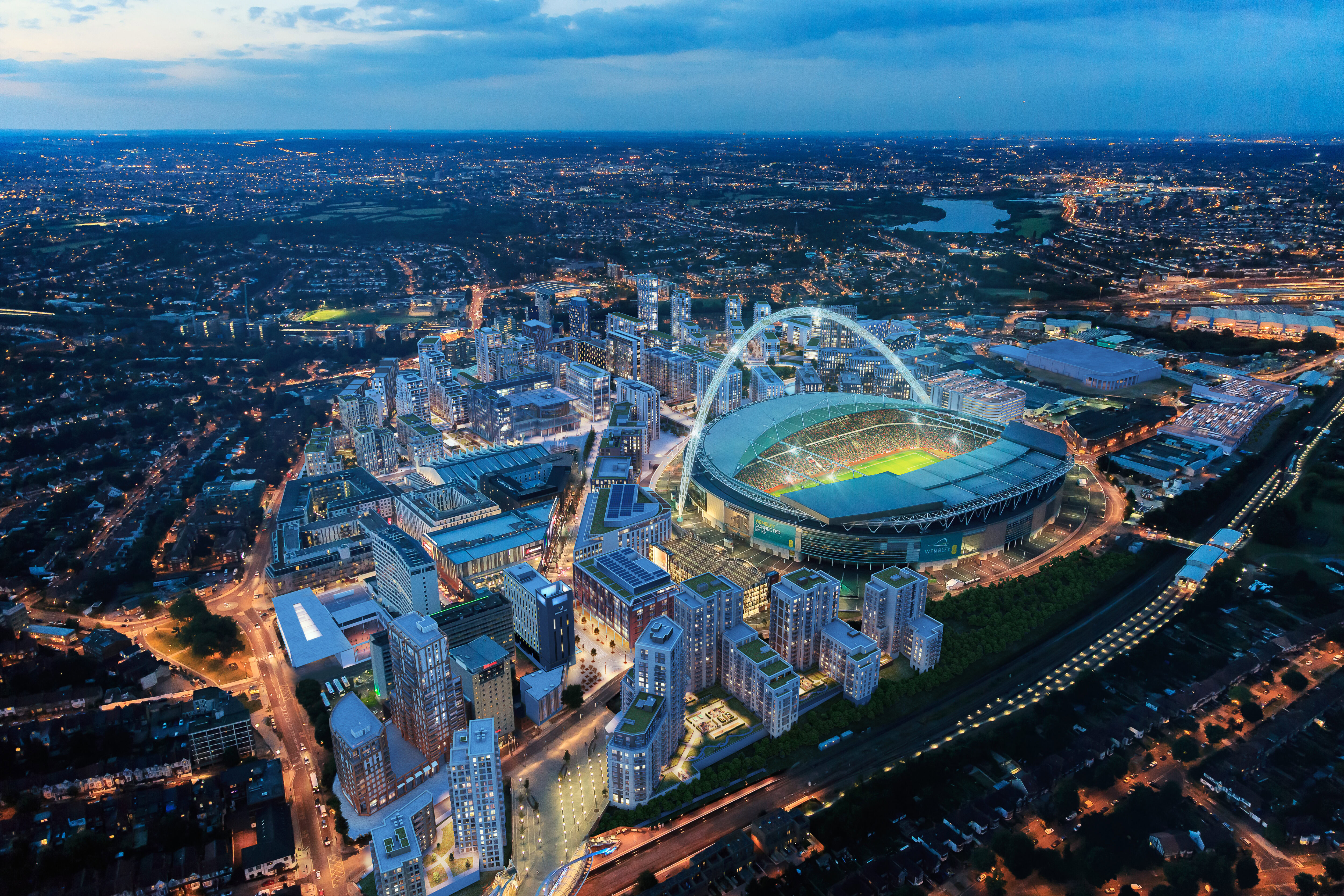 A sold out Wembley stadium surrounded by a large amount of modern high top and low top buildings with lights on at night.