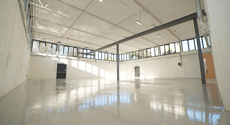 A large empty warehouse with a large empty space. White painted walls with 3 doors for entering and exiting.
