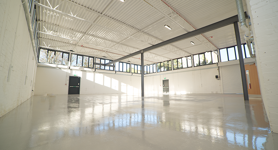 A large empty warehouse with a large empty space. White painted walls with 3 doors for entering and exiting.