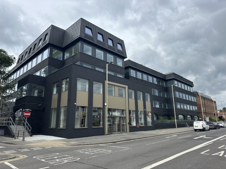 A building with windows along the side of a road, set against a backdrop of the sky and clouds, surrounded by vehicles and signs of a mixed-use urban neighborhood.