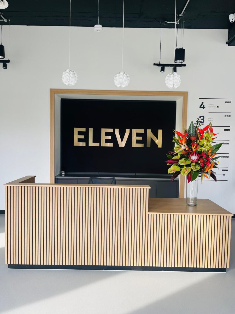 A desk with a vase of flowers in front of a computer screen, surrounded by indoor plants and designed for interior aesthetics.