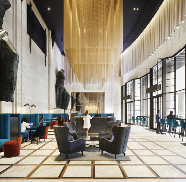 A group of people gathered in a room with various furniture, including a couch, chairs, and a coffee table. The space features windows and has an inviting interior design.