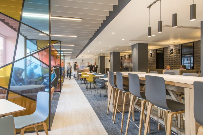 A spacious room featuring several tables and chairs arranged for dining, with a ceiling overhead and walls surrounding the area. The floor is designed for indoor use, making it suitable for a cafeteria or restaurant setting.