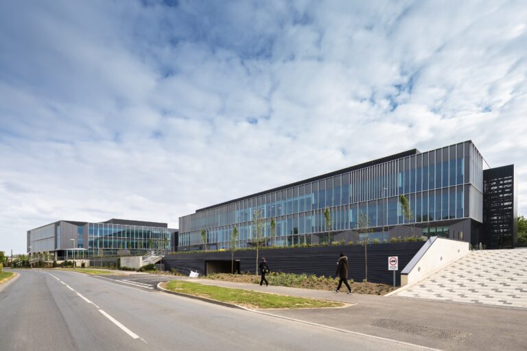 A large commercial building with glass walls, set against a backdrop of a blue sky with clouds. The environment appears to be outdoors, featuring an empty road in front of the structure.
