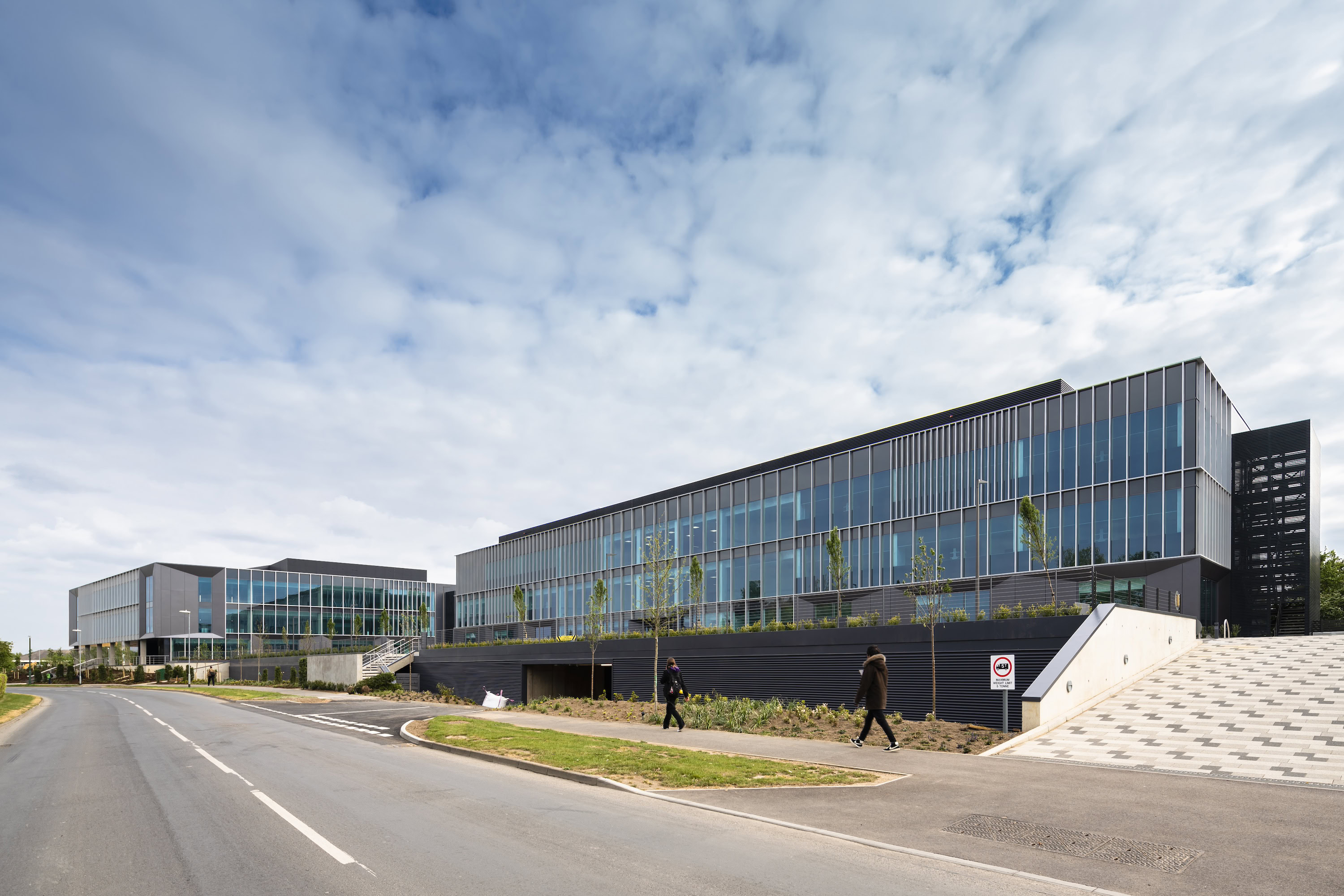 A large commercial building with glass walls, set against a backdrop of a blue sky with clouds. The environment appears to be outdoors, featuring an empty road in front of the structure.
