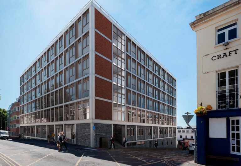 A large commercial building with numerous windows, set against a clear sky, located along a city street. The structure features a mixed-use facade and represents architectural design in an urban environment.