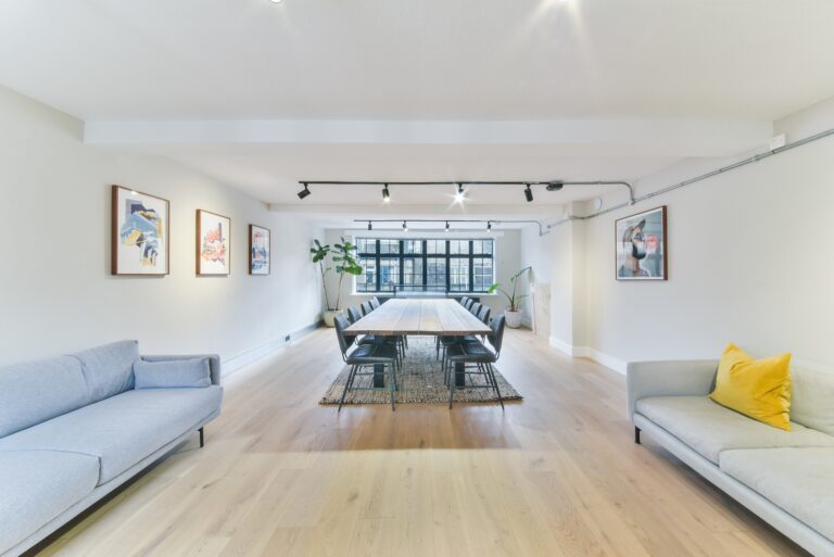 A cozy living room featuring a table surrounded by couches, with a warm and inviting atmosphere. The space includes hardwood flooring and comfortable furnishings, making it ideal for relaxation or social gatherings.