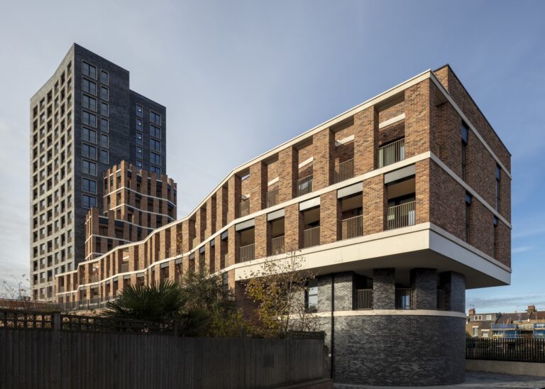 A commercial building with a facade and multiple windows, surrounded by a fence. The structure is situated in an urban area, showcasing brutalist architecture against a clear sky.