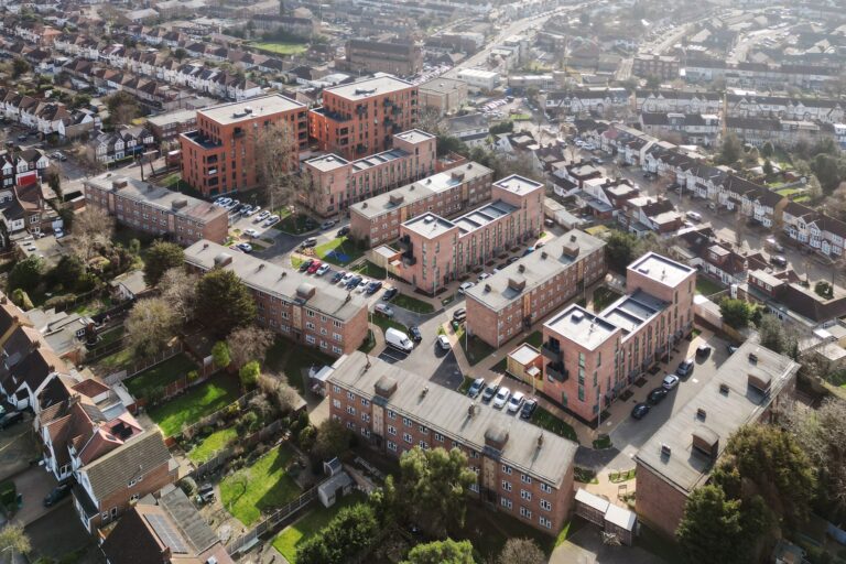 Aerial view of a city showcasing numerous buildings, with a mix of residential areas and urban design. Trees punctuate the landscape in this suburban neighborhood.