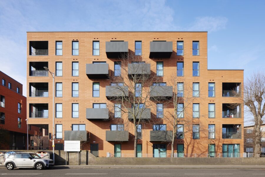 A building with numerous windows, surrounded by trees and parked cars, set against a clear sky in an urban environment.
