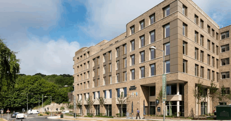 Modern multi-storey student accommodation building with "Student Roost" signage, located on a tree-lined street under a partly cloudy sky.