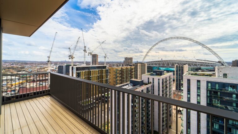A bridge with a handrail and deck, overlooking a city filled with buildings against a backdrop of clouds and sky.