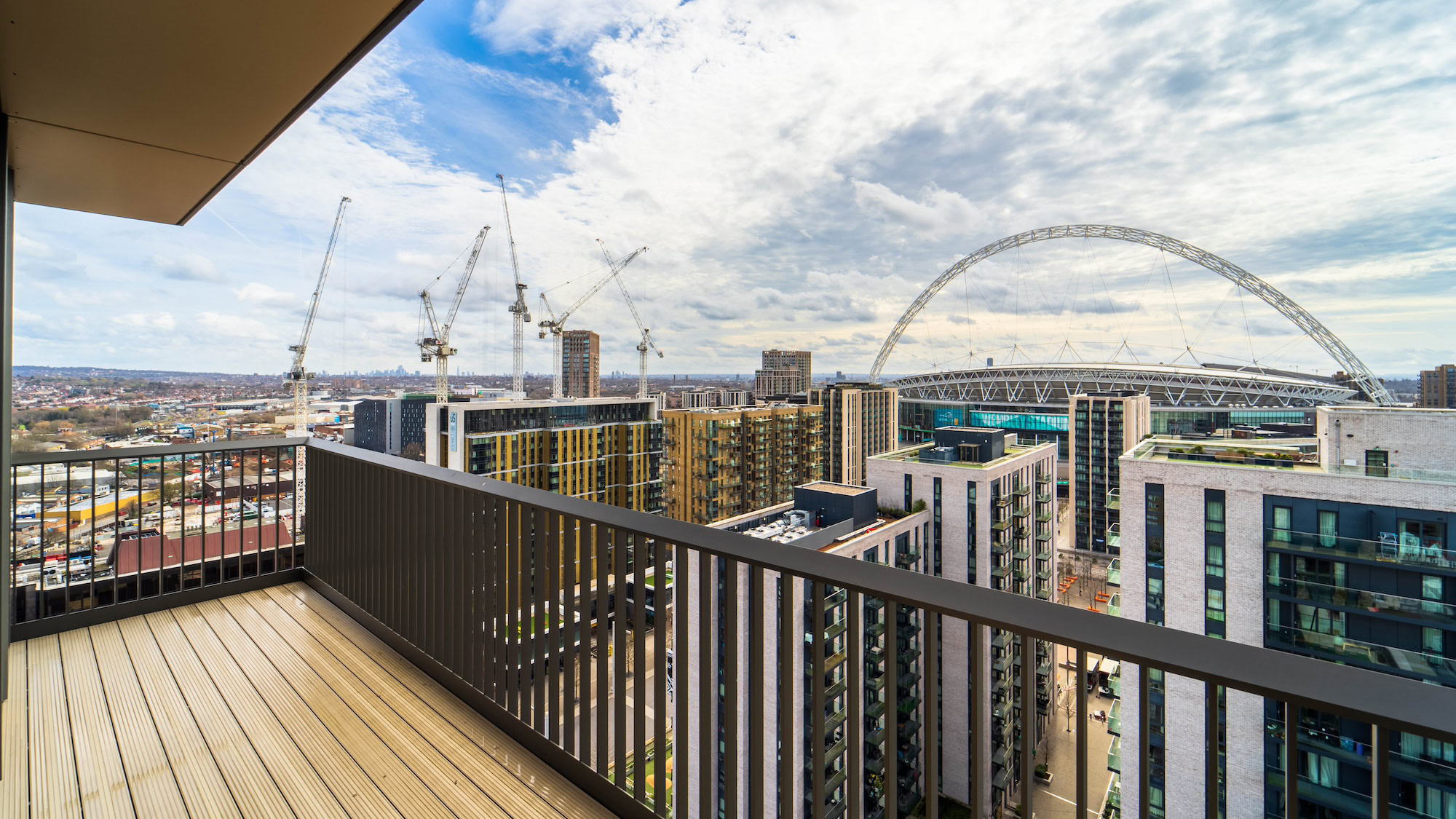 A bridge with a handrail and deck, overlooking a city filled with buildings against a backdrop of clouds and sky.