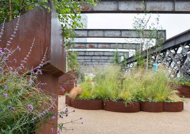 A rustic urban garden with steel planters and wildflowers under rusted metal beams.