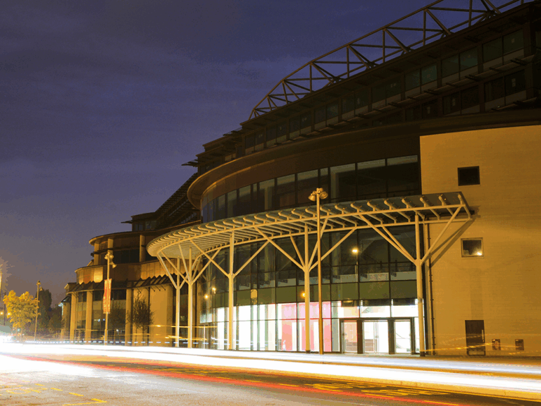Image of the exterior of Twickenham Stadium at night showing the front entrance lit up
