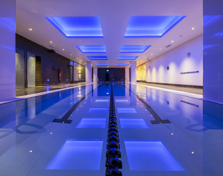 An indoor swimming pool with blue lighting, featuring a lane divider in the middle.