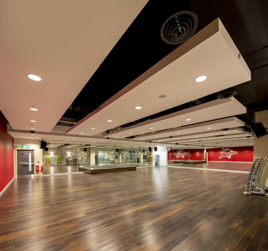 A spacious gym studio with wooden floors, red and white walls, and ceiling lights.