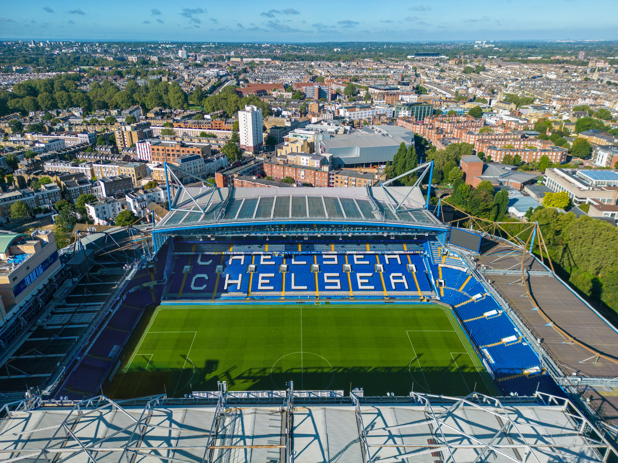 Aerial view of a sports stadium featuring a green field, surrounded by urban buildings under a clear sky.