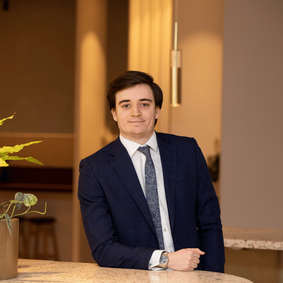 Man in a dark blue suit with a patterned tie leaning on a marble counter in a modern indoor setting.