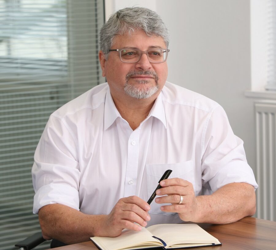 Man in white shirt sitting with pen in hand and notebook in front of him
