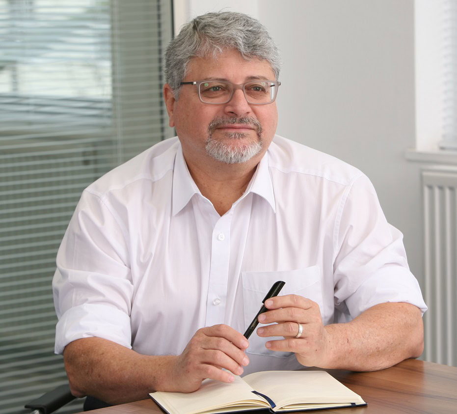Man in white shirt sitting with pen in hand and notebook in front of him