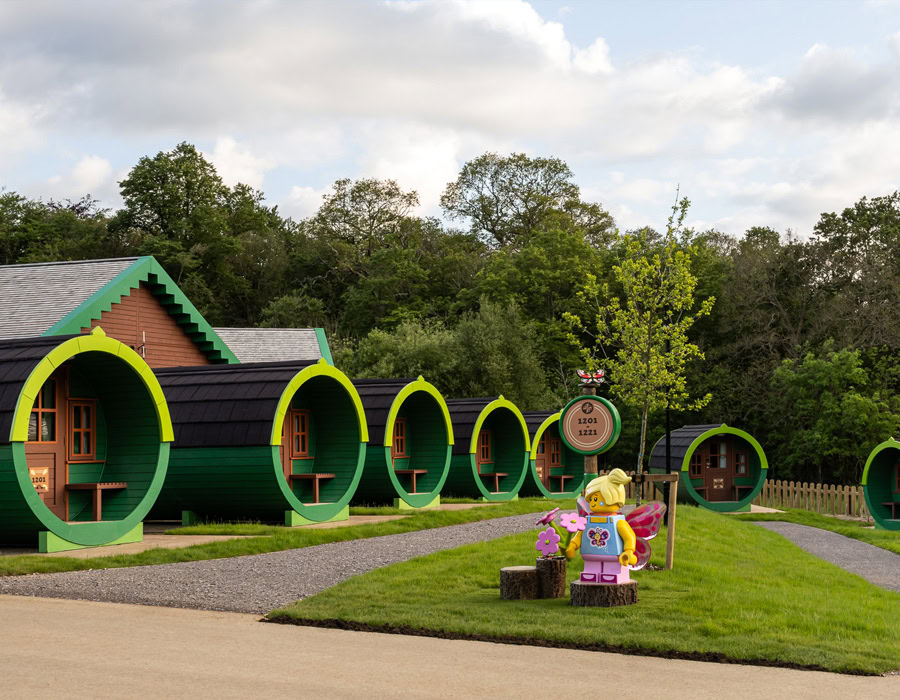 A collection of round cabins with fluroscent green frames in the heart of a lush greeen setting. A LEGO statue on the grass, adding a touch