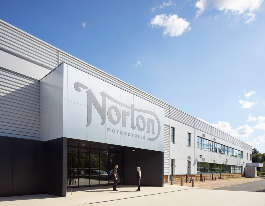 A modern new buiidng with "Norton Motorcycles" logo on the facade. Two people are standing at the front of the entrance.