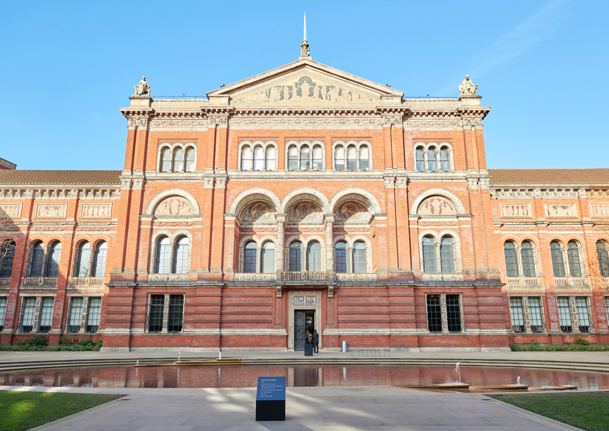 A large red-brick building with arched windows, a main entrance, featuring a courtyard and a reflective pool at the front