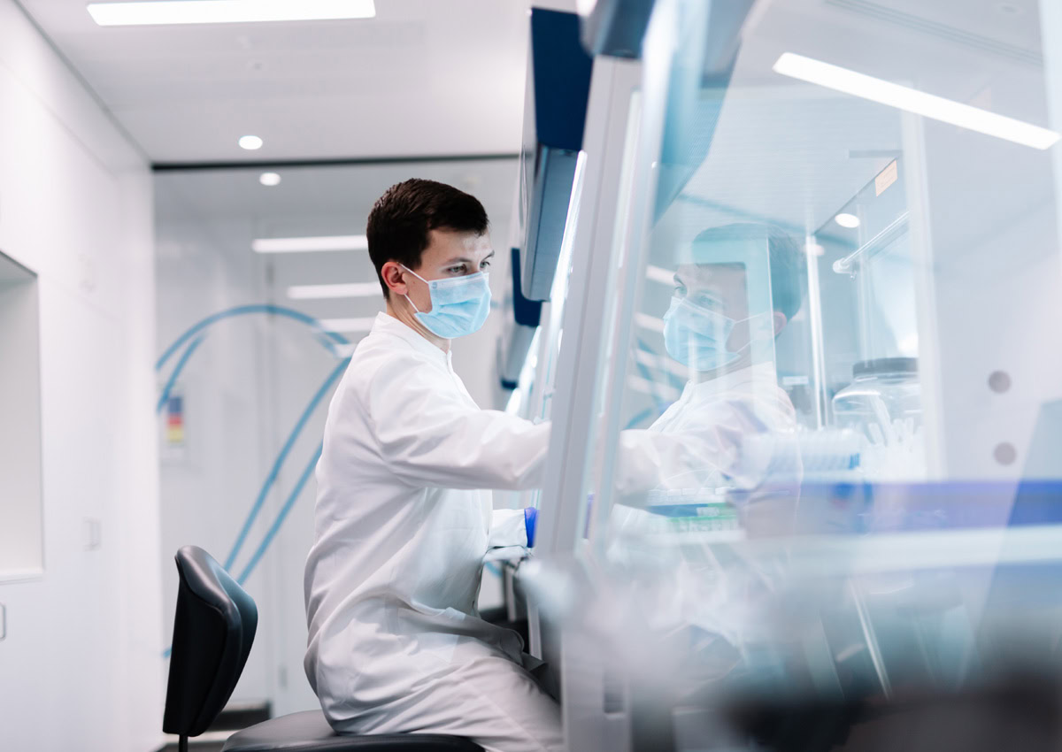 A scientist in a lab coat with a mask working intently at a lab bench, surrounded with sterile equipment, conveying focus, precision and dedication in a new modern lab.
