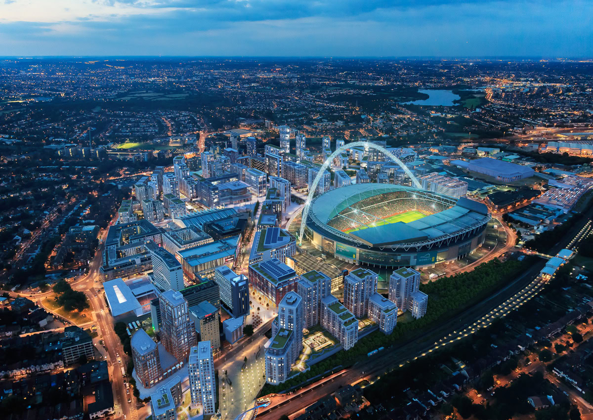 Aerial view of a brightly lit Wembly Stadium, surrounded by corporate buildings. The skyline reaches into the horizon, portraying energy and excitement.