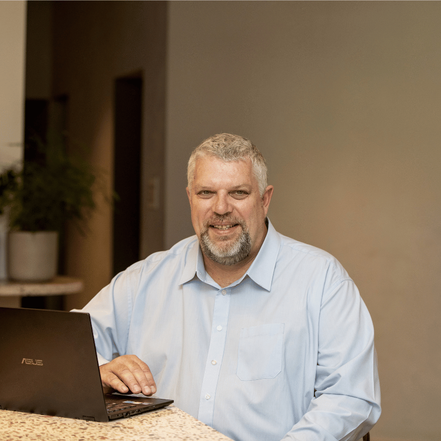 Man wearing a light blue shirt seated at a terrazzo countertop with an open laptop in front of him.