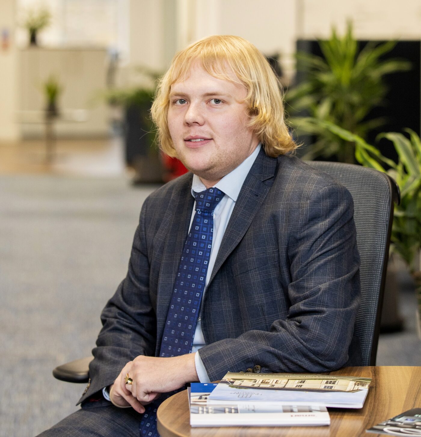 Man in blue suit sitting at a table in an office with magazines in front of him