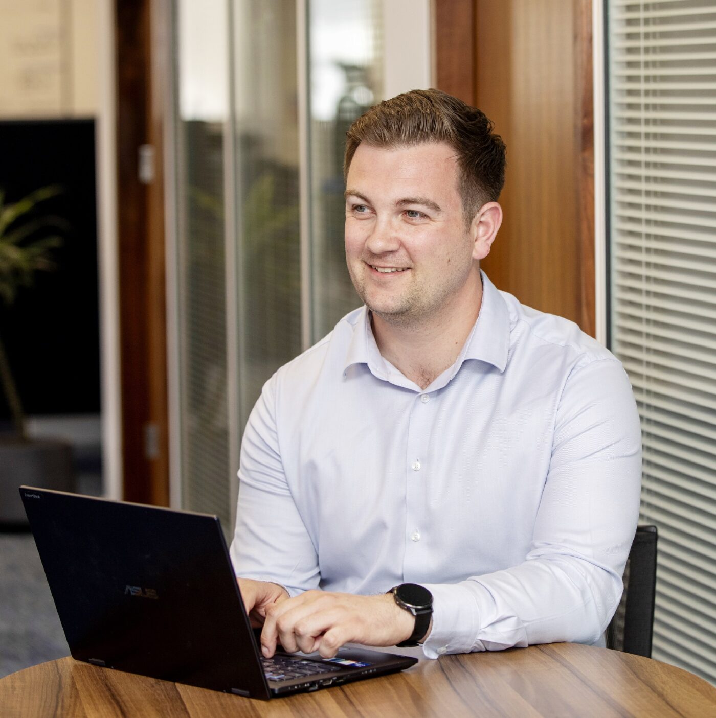 Man Sitting at laptop with office in the background