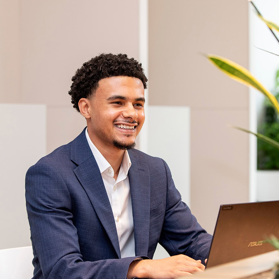 Photo of man in a suit smiling with a laptop in front of him.
