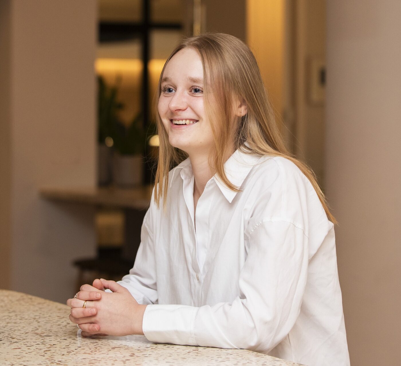 Woman in white shirt smiling out of shot, leaning on desktop in corporate setting