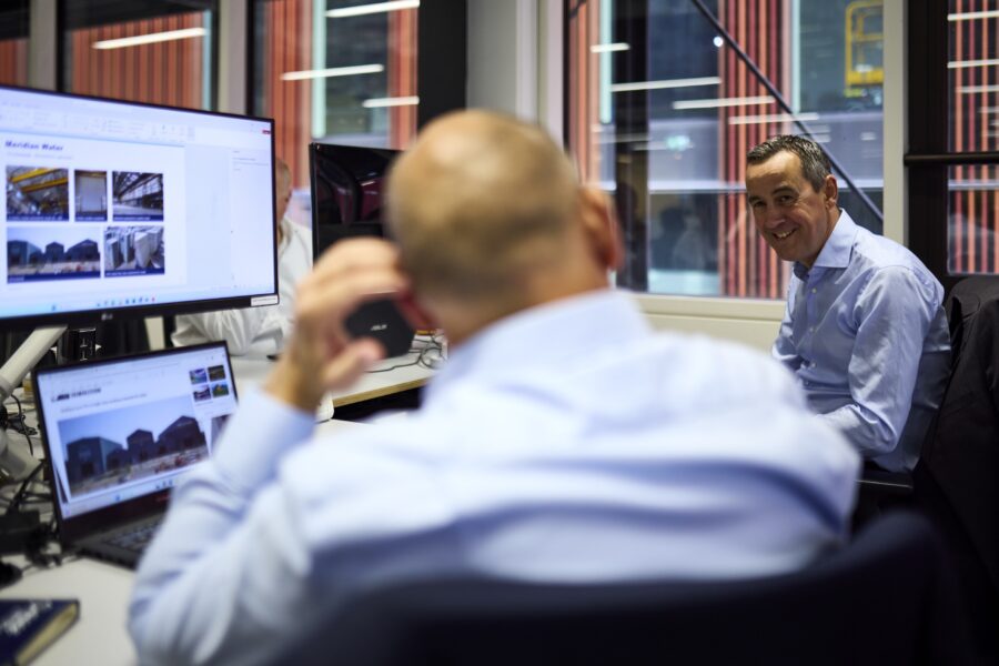 Two men having a discussion whilst sitting at their desks looking at project imagery.