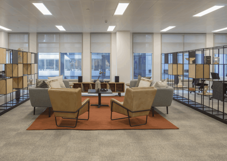 Modern office space with neutral-toned seating, shelves, and large windows.