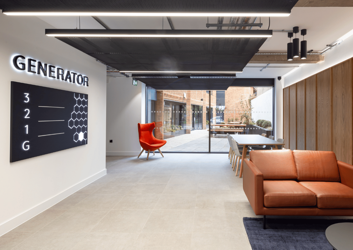 Modern office lounge featuring a burnt orange sofa, red high-back chair, and long communal table with chairs.