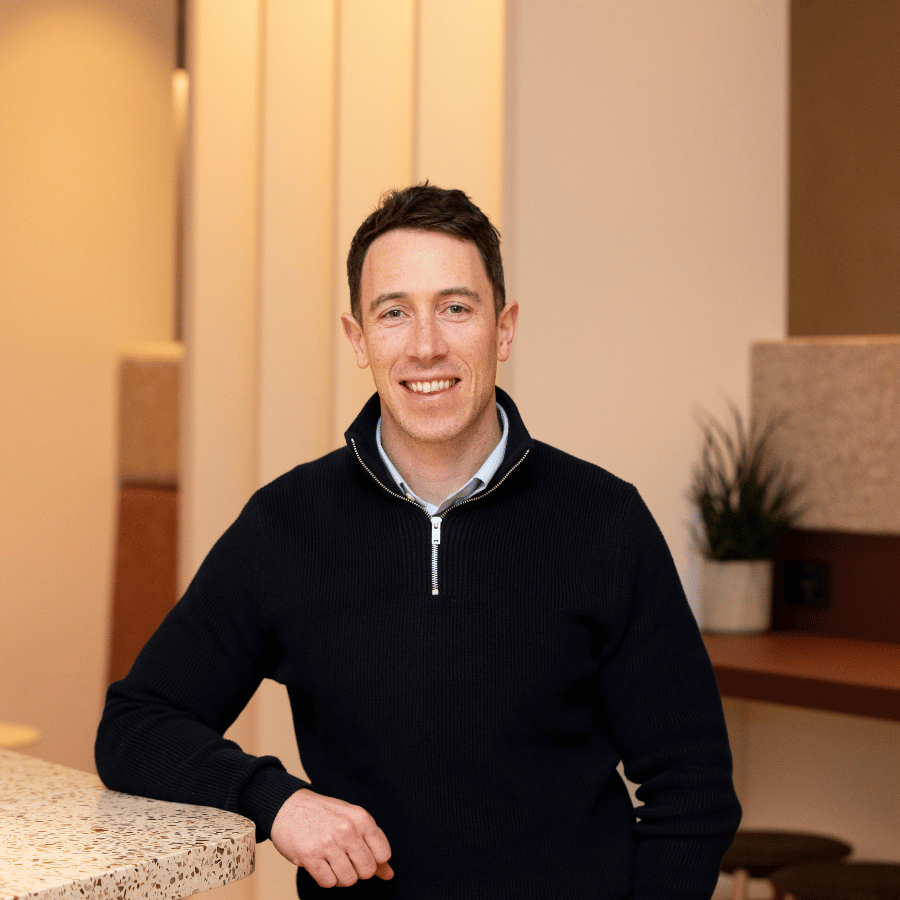 Man wearing a navy sweater leaning on a countertop in a modern indoor space.