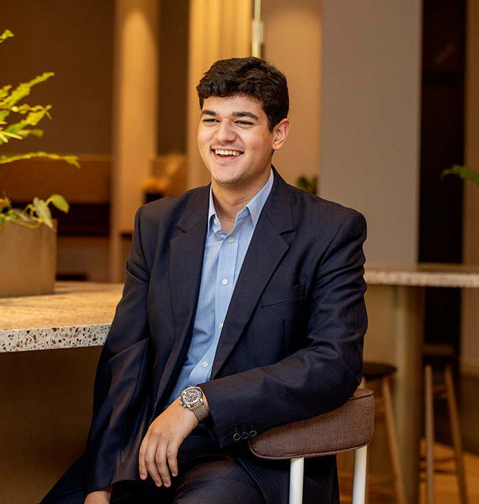 Man in dark suit with blue shirt on, laughing off camera in a corporate setting