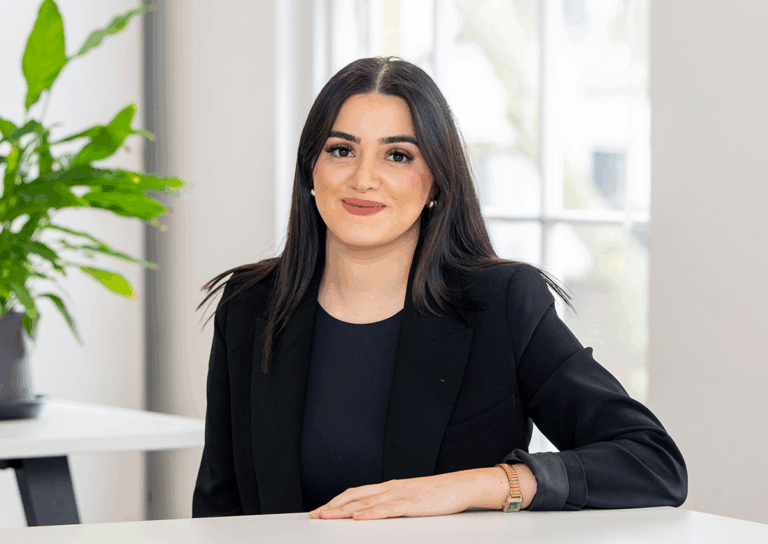 Woman in black dress and black suit jacket leaning arm on the table, smiling to the camera