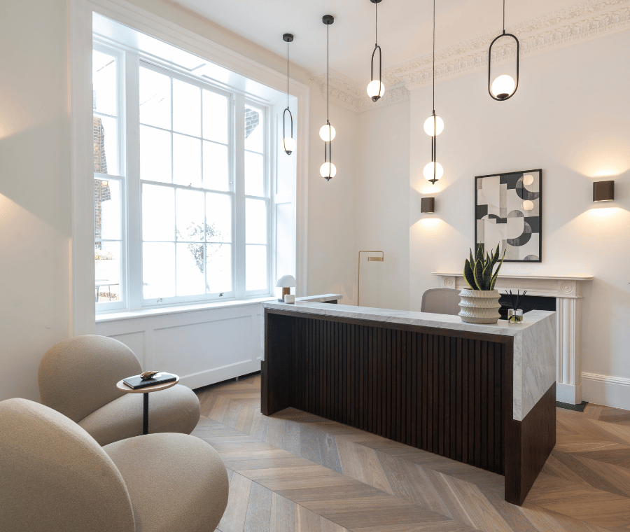 Modern reception area with a dark wood desk, light chairs, pendant lights, and large window.