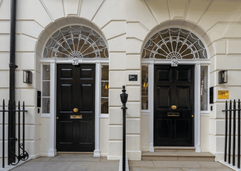Two adjacent black front doors numbered 27 and 29, set in cream-colored arched doorways with decorative fanlights above.