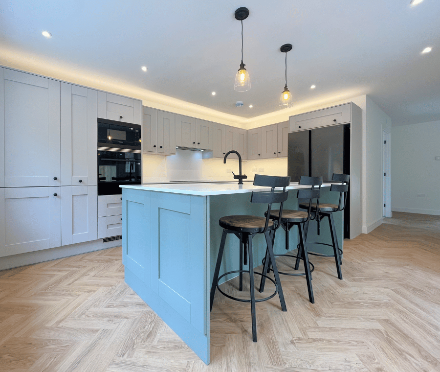 Modern kitchen with light grey cabinets, blue island, black bar stools, and pendant lights.
