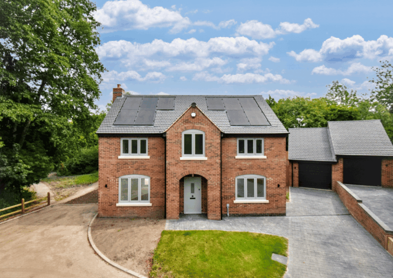 Red-brick detached house with solar panels on the roof, grey driveway, and attached garage, surrounded by greenery.